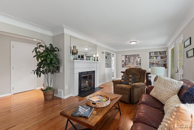 603 Outer Dr, Tecumseh, MI 49286 - living room featuring wood finished floors, built in shelves, a fireplace with flush hearth, baseboards, and crown molding