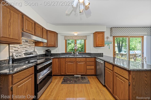 1145 W Moore Rd, Milford, MI 48381 - kitchen featuring stainless steel appliances, under cabinet range hood, a peninsula, light wood-style floors, and brown cabinetry