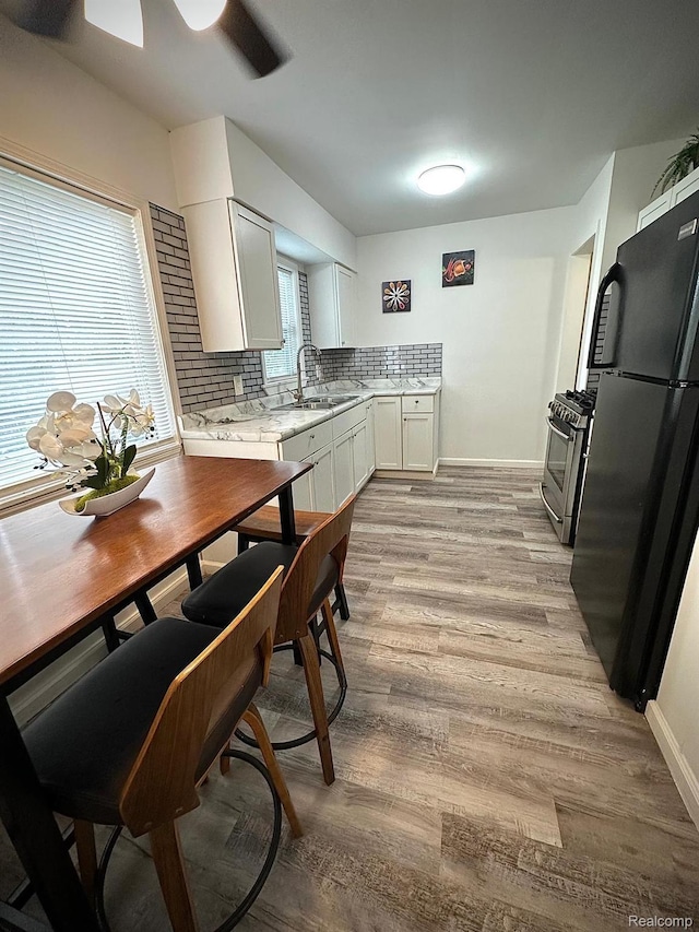2825 Raskob St, Flint, MI 48504 - kitchen featuring freestanding refrigerator, stainless steel gas stove, a sink, light wood finished floors, and decorative backsplash