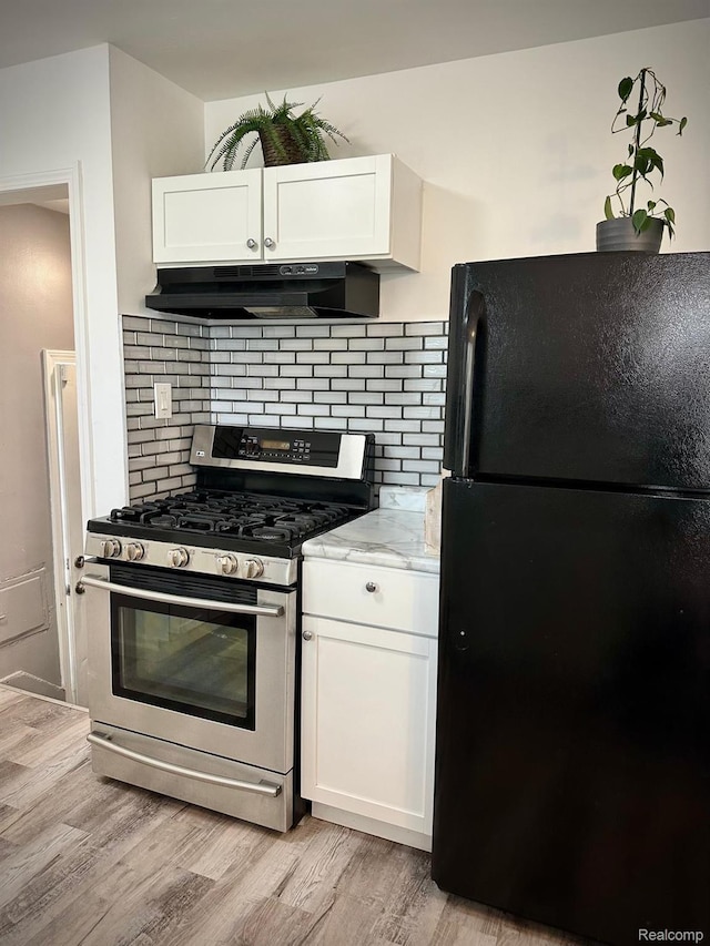 2825 Raskob St, Flint, MI 48504 - kitchen with freestanding refrigerator, stainless steel gas range oven, under cabinet range hood, white cabinets, and backsplash