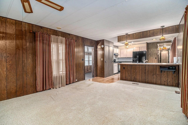 180 Bonnie St, Ludington, MI 49431 - kitchen featuring black fridge, ceiling fan, stainless steel range with gas stovetop, wood walls, and light carpet