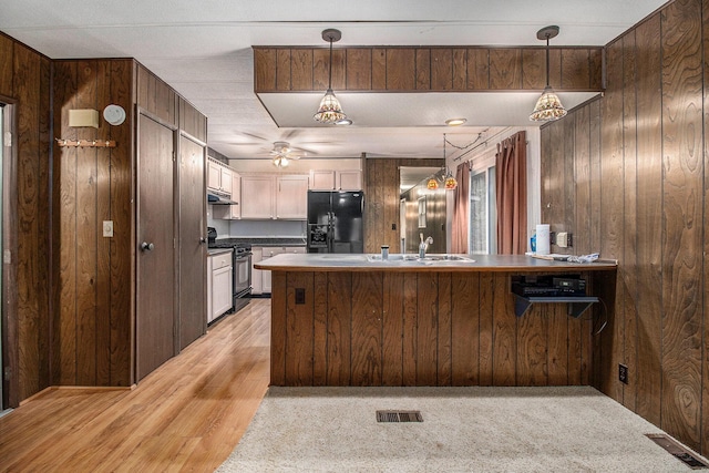 180 Bonnie St, Ludington, MI 49431 - kitchen with black appliances, a peninsula, wood walls, under cabinet range hood, and hanging light fixtures