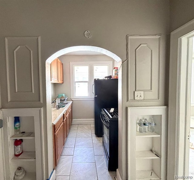 2340 Clements St, Detroit, MI 48238 - kitchen with black gas stove, arched walkways, light countertops, brown cabinetry, and baseboards