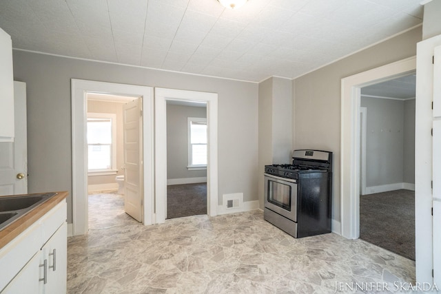 884 Emerson Ave, Muskegon, MI 49442 - kitchen featuring gas range, white cabinetry, stone finish flooring, baseboards, and crown molding