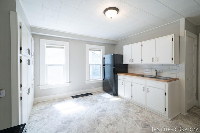 884 Emerson Ave, Muskegon, MI 49442 - kitchen with a sink, freestanding refrigerator, white cabinets, decorative backsplash, and baseboards