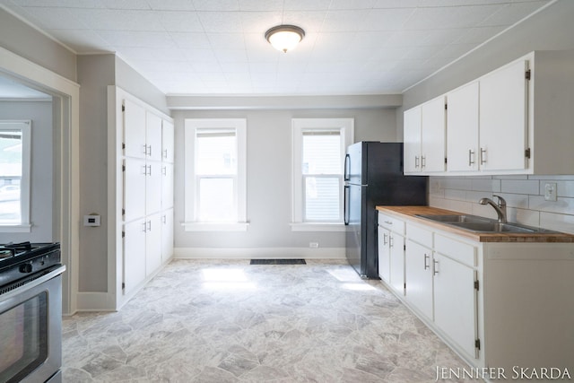 884 Emerson Ave, Muskegon, MI 49442 - kitchen featuring stainless steel range with gas stovetop, freestanding refrigerator, white cabinetry, a sink, and decorative backsplash