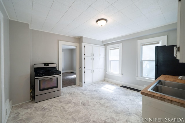 884 Emerson Ave, Muskegon, MI 49442 - kitchen featuring gas range, freestanding refrigerator, a sink, white cabinets, and baseboards