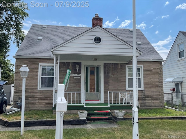 6250 Grandville Ave, Detroit, MI 48228 - view of front facade with stone siding, a shingled roof, a chimney, and covered porch