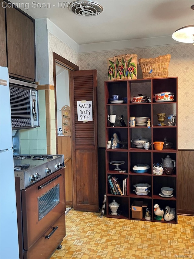 6250 Grandville Ave, Detroit, MI 48228 - kitchen with stove, stainless steel microwave, freestanding refrigerator, wallpapered walls, and open shelves