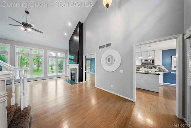 8487 Sherwood Dr, Grosse Ile, MI 48138 - unfurnished living room with high vaulted ceiling, a ceiling fan, wood finished floors, stairs, and baseboards