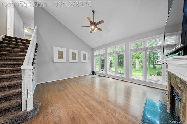 8487 Sherwood Dr, Grosse Ile, MI 48138 - unfurnished living room featuring a ceiling fan, a stone fireplace, high vaulted ceiling, stairs, and wood finished floors
