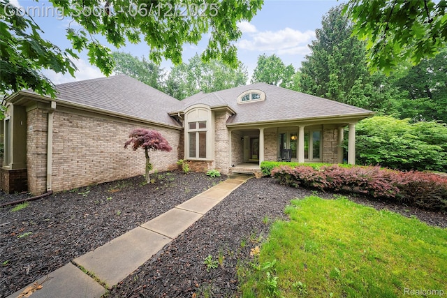 8487 Sherwood Dr, Grosse Ile, MI 48138 - french country home with brick siding, a porch, and roof with shingles