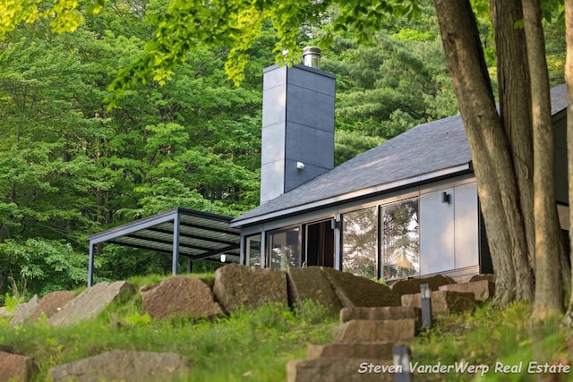 5185 W Nurnberg Rd, Michigan, MI 49411 - back of house with a chimney, a forest view, and roof with shingles