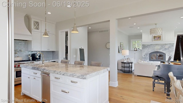 571 Dunleavy Dr, Highland, MI 48356 - kitchen with wall chimney range hood, high end range, open floor plan, tasteful backsplash, and light wood finished floors