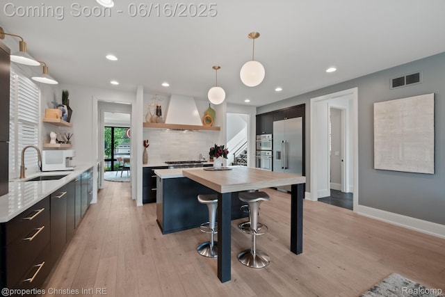 1044 Hazel, Birmingham, MI 48009 - kitchen featuring open shelves, custom exhaust hood, appliances with stainless steel finishes, light wood-style flooring, and pendant lighting