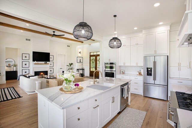 2958 S Edgar Rd, Mason, MI 48854 - kitchen featuring appliances with stainless steel finishes, a sink, a lit fireplace, white cabinets, and light wood finished floors