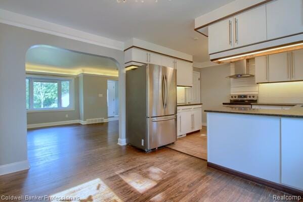 25811 Briarbank Ave, Southfield, MI 48033 - kitchen with appliances with stainless steel finishes, arched walkways, wall chimney range hood, dark countertops, and white cabinetry