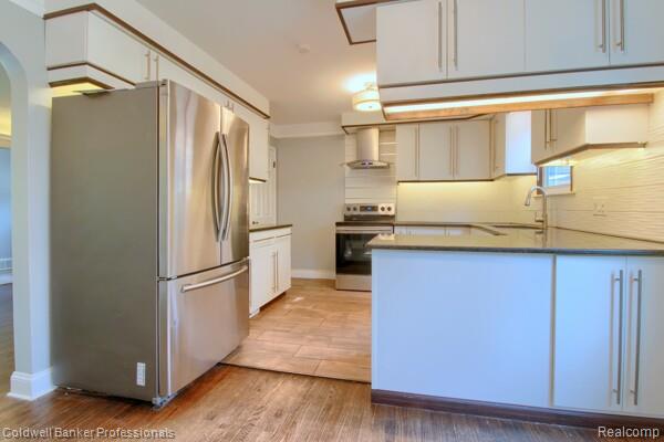 25811 Briarbank Ave, Southfield, MI 48033 - kitchen with appliances with stainless steel finishes, wall chimney range hood, arched walkways, light wood-style flooring, and a peninsula