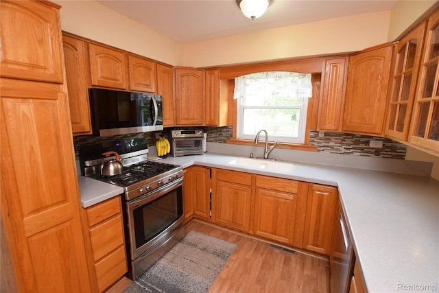 5483 Ameno Ln, Swartz Creek, MI 48473 - kitchen with stainless steel gas range oven, a sink, decorative backsplash, and light wood-style floors