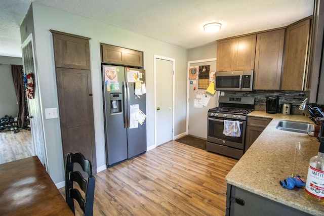 7070 Quain Rd, Birch Run, MI 48415 - kitchen with stainless steel appliances, a sink, light wood-style flooring, decorative backsplash, and baseboards