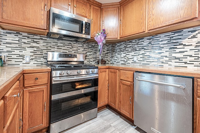 2110 Saint Charles Ave SW, Grand Rapids, MI 49507 - kitchen with stainless steel appliances, light wood finished floors, tasteful backsplash, light countertops, and brown cabinets
