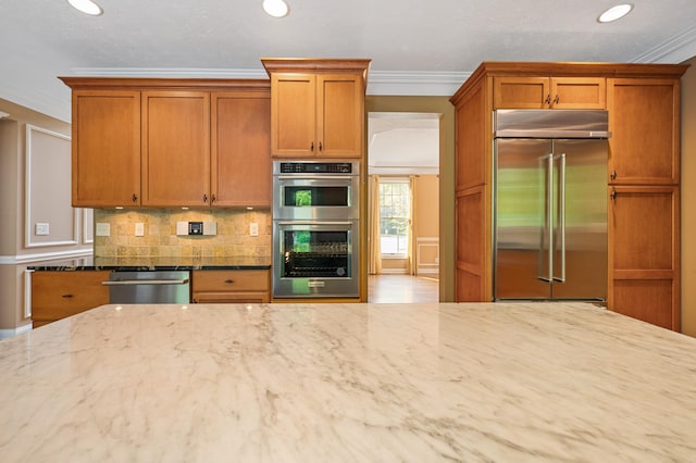 3265 Estates Dr, Saint Joseph, MI 49085 - kitchen with appliances with stainless steel finishes, ornamental molding, light stone counters, decorative backsplash, and brown cabinetry