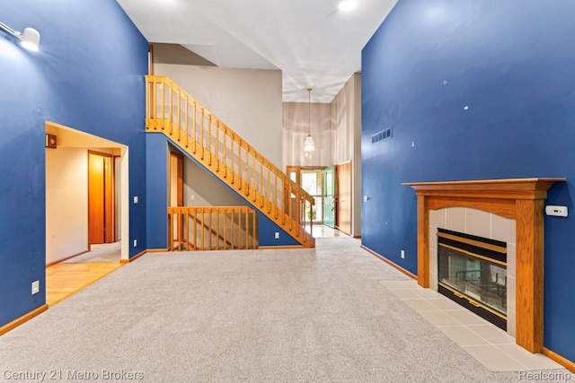 751 River Edge Ct, Flushing, MI 48433 - unfurnished living room with a towering ceiling, carpet floors, stairs, and a tile fireplace