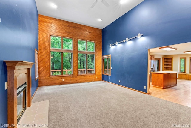 751 River Edge Ct, Flushing, MI 48433 - unfurnished living room featuring ceiling fan, wooden walls, a tile fireplace, carpet flooring, and a towering ceiling