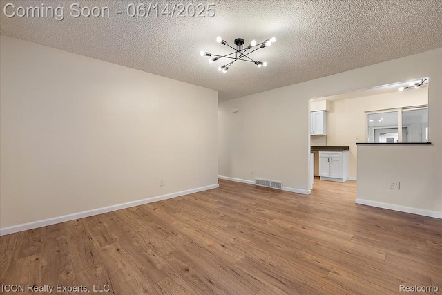 2570 Tarry Dr, Macomb, MI 48310 - unfurnished living room with a chandelier, light wood-type flooring, baseboards, and a textured ceiling