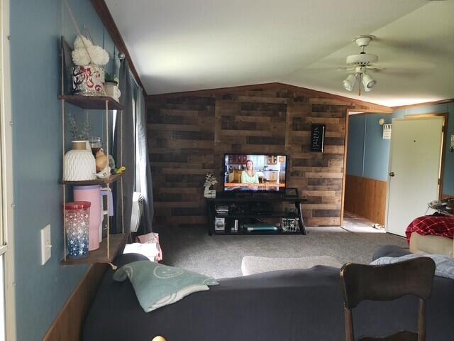 15754 N 10th Ave, Marion, MI 49665 - carpeted living room with wood walls, vaulted ceiling, and a ceiling fan