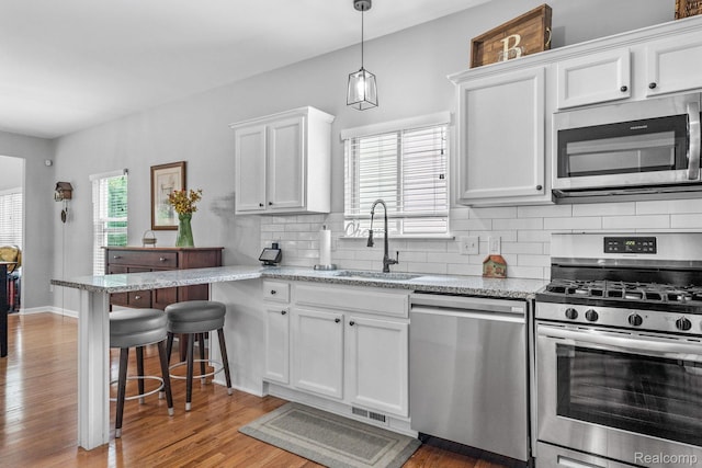 1156 Fairway Dr, Pontiac, MI 48340 - kitchen with stainless steel appliances, white cabinetry, backsplash, light wood-type flooring, and a kitchen bar
