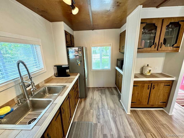 3840 Beech St, Burtchville, MI 48059 - kitchen featuring black microwave, brown cabinetry, freestanding refrigerator, light wood-style flooring, and light countertops