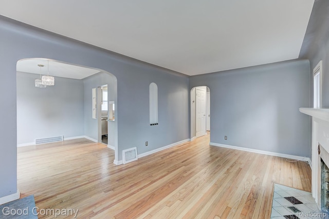 263 E Woodland St, Ferndale, MI 48220 - unfurnished living room featuring arched walkways, light wood-style flooring, a fireplace with flush hearth, and a chandelier