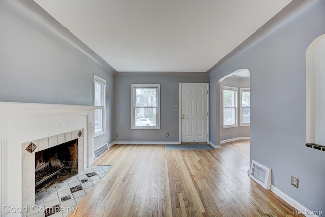263 E Woodland St, Ferndale, MI 48220 - unfurnished living room with arched walkways, light wood-style flooring, a tiled fireplace, and healthy amount of natural light