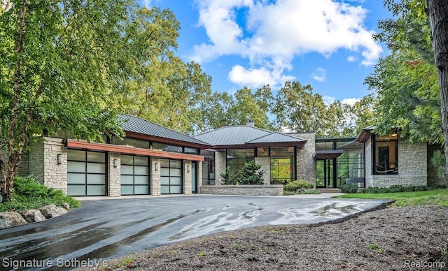 6956 Cooley Lake Rd, White Lake, MI 48383 - view of front of property featuring stone siding, metal roof, asphalt driveway, a standing seam roof, and an attached garage
