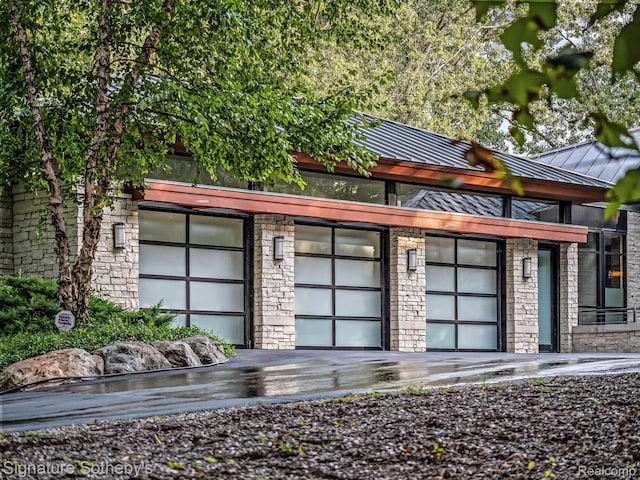 6956 Cooley Lake Rd, White Lake, MI 48383 - view of front of house with stone siding, a standing seam roof, a garage, metal roof, and driveway