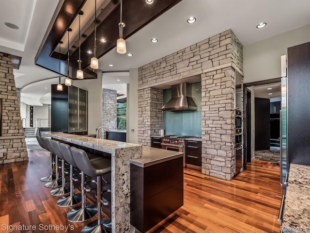 6956 Cooley Lake Rd, White Lake, MI 48383 - kitchen with decorative columns, wall chimney range hood, dark wood finished floors, a breakfast bar, and recessed lighting