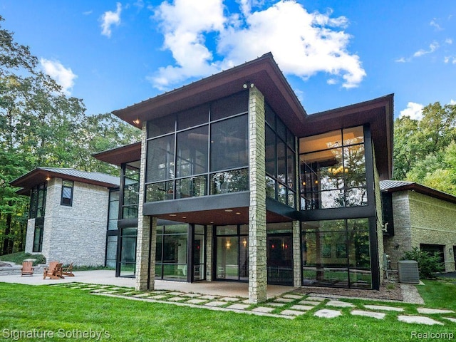 6956 Cooley Lake Rd, White Lake, MI 48383 - rear view of house featuring a sunroom, a patio, stone siding, and metal roof
