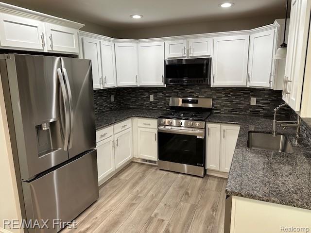 33315 Vista Way, Fraser, MI 48026 - kitchen with appliances with stainless steel finishes, a sink, white cabinets, light wood-style floors, and dark stone countertops