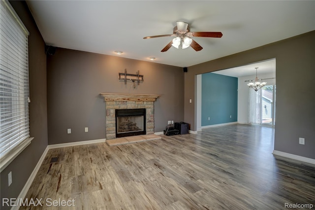 11468 Grand Oaks Dr, Clio, MI 48420 - unfurnished living room featuring a stone fireplace, ceiling fan, wood finished floors, a chandelier, and baseboards