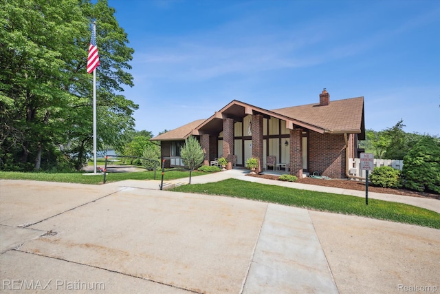12132 Lexington Dr Unit 2, South Lyon, MI 48178 - mid-century modern home featuring a chimney, brick siding, roof with shingles, and a front lawn