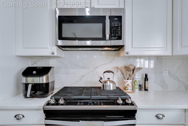 30753 Sunderland Dr, Farmington Hills, MI 48331 - kitchen featuring stainless steel microwave, black range with gas stovetop, white cabinets, and decorative backsplash