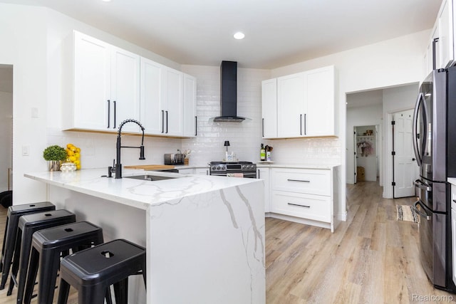 62874 Walker Ct Unit 17, Washington, MI 48094 - kitchen featuring wall chimney exhaust hood, a peninsula, stainless steel appliances, light wood-type flooring, and a kitchen bar