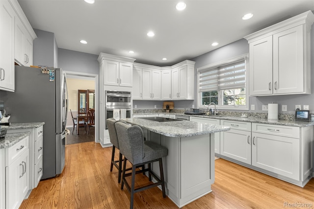 4991 Knollcrest Ct, Commerce Twp, MI 48382 - kitchen featuring stainless steel appliances, white cabinetry, a kitchen breakfast bar, light wood-type flooring, and recessed lighting