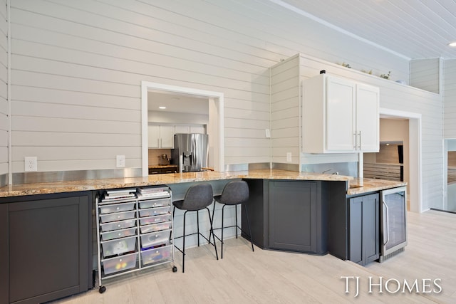 2605 Shadowbrook Dr SE, Grand Rapids, MI 49546 - kitchen featuring stainless steel refrigerator with ice dispenser, beverage cooler, white cabinets, wood walls, and light stone counters