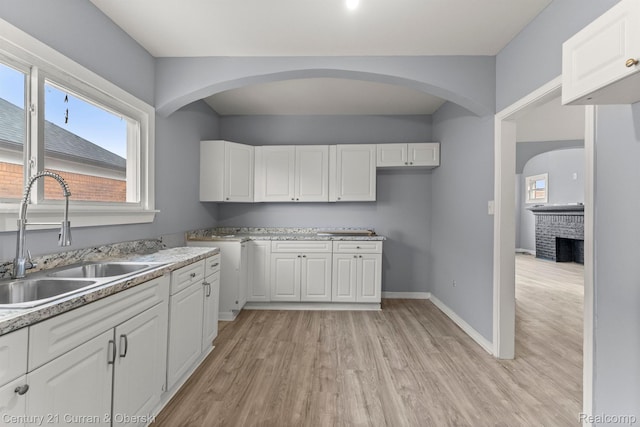 2633 Monterey St, Detroit, MI 48206 - kitchen with a sink, light wood-type flooring, white cabinetry, a fireplace, and baseboards