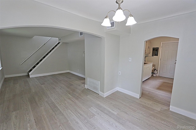 19444 Inkster Rd, Redford, MI 48240 - empty room with arched walkways, light wood finished floors, baseboards, stairs, and a chandelier