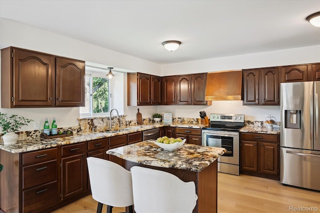 5695 Deerwood, Commerce Twp, MI 48382 - kitchen with stainless steel appliances, custom range hood, a breakfast bar area, light stone counters, and light wood-type flooring