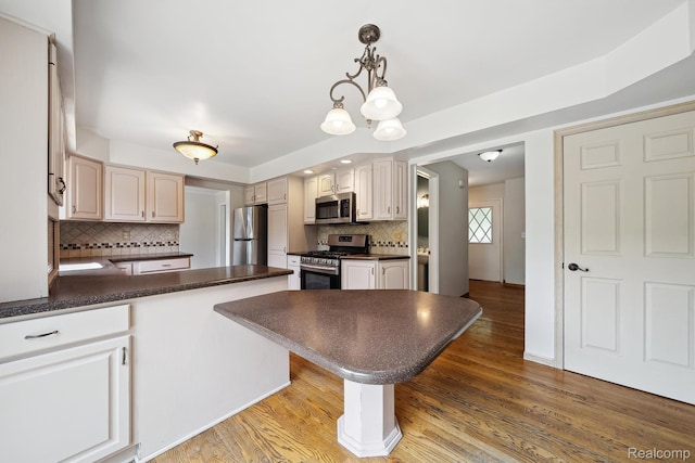 7302 Parkway Ct, Canton, MI 48187 - kitchen with appliances with stainless steel finishes, dark countertops, a peninsula, backsplash, and light wood-style flooring