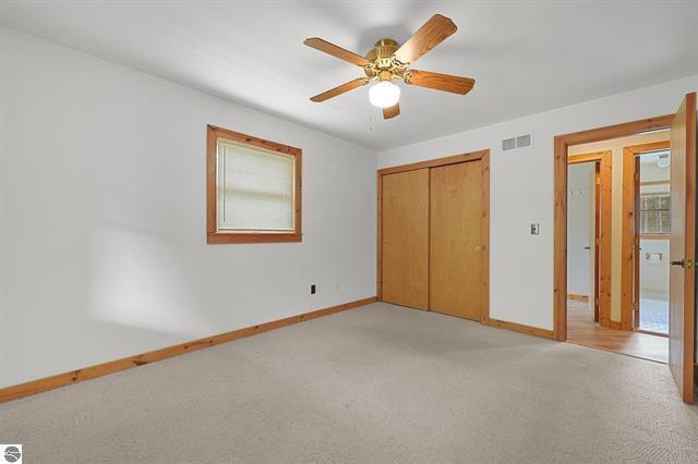 2460 E 26th Rd, Cadillac, MI 49601 - unfurnished bedroom with light colored carpet, baseboards, a closet, and a ceiling fan
